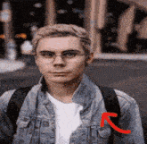 a young man wearing glasses and a denim jacket has a red arrow pointing to his left