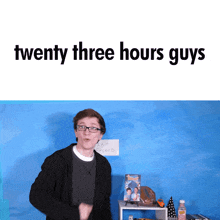 a man with glasses is standing in front of a blue wall with the words twenty three hours guys