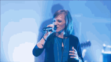 a woman singing into a microphone in front of a blue backdrop