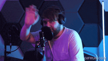 a man wearing headphones stands in front of a microphone with gifrun.com written on the bottom right