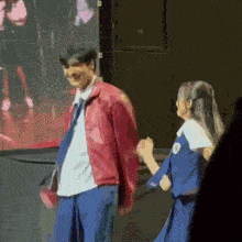 a man in a red jacket is standing next to a woman in a blue dress holding hands .
