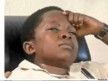 a young boy is sitting in a chair with his hand on his head .