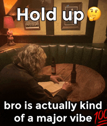 a man sits at a table with a bottle of beer and a book and says " hold up " on the top