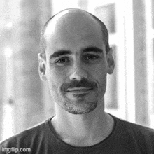 a black and white photo of a bald man with a beard smiling .