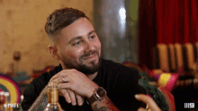 a man with a beard is sitting at a table with a bottle of whiskey and the number 9 on the bottom left