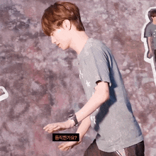 a man wearing a gray shirt with a watch on his wrist is standing in front of a wall with korean writing on it