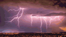 lightning strikes over a city at night with purple clouds