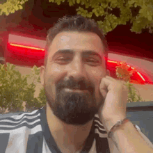 a man with a beard and a striped shirt is smiling and holding his hand to his face .