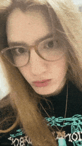 a girl wearing glasses and a necklace is looking at the camera .