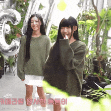 two girls are standing in front of a large number 3