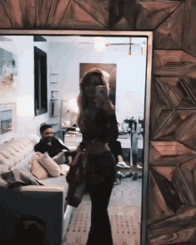 a woman taking a picture of herself in a mirror while a man sits on a couch in the background
