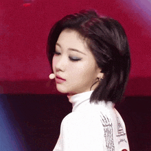 a woman wearing a white turtleneck and a microphone looks to the side