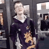 a young man wearing a purple hoodie with a wolf on it is standing in front of a door .