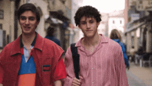 two young men are walking down a street and one of them is wearing a pink shirt
