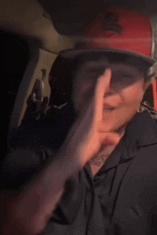 a man wearing a red hat and a black shirt is making a funny face while sitting in a car .
