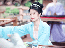 a woman in a blue dress is sitting at a table with a cup on it