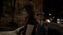 a man in a suit and hat talks to a woman