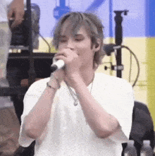 a young man is singing into a microphone while standing on a stage .