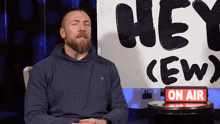 a man sitting in front of a sign that says " hey crew "
