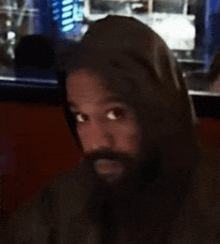 a man with a beard wearing a hoodie is sitting in a restaurant .