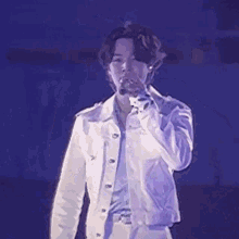 a man in a white jacket is holding a microphone in his hand and singing into it .