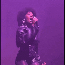 a woman in a leather jacket is singing into a microphone on a stage .