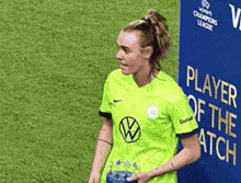 a female soccer player is standing in front of a player of the match sign .