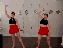 two women in red skirts are dancing in front of balloons that spell out roar