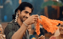 a man is smiling while holding a garland of flowers in his hands .