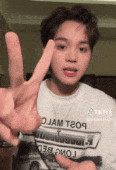 a young man wearing a shirt that says ojam t209 giving a peace sign