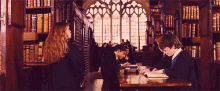 a group of people are sitting at a table in a library with books on it .