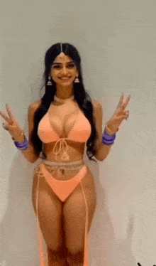 a woman in a bikini is standing in front of a white wall giving a peace sign .