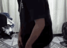 a man in a black shirt is standing on a tile floor in a room .