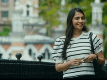 a woman in a black and white striped shirt smiles while holding a cell phone