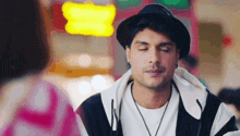 a man wearing a hat and a striped jacket is sitting in front of a woman with his eyes closed .