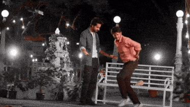 two men are standing next to each other on a park bench at night