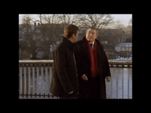 a man in a black jacket stands on a bridge over a body of water