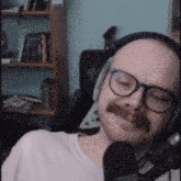 a man with glasses and a mustache is sitting in front of a microphone