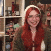 a woman with red hair and glasses is smiling in front of a shelf full of dolls .