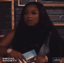 a woman in a black hijab is talking to someone in front of a wall with gold frames and the words social society on it
