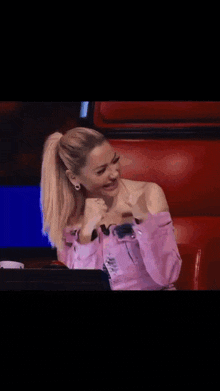 a woman in a pink off the shoulder top is laughing while sitting in a chair .