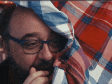 a man wearing glasses and a plaid shirt covering his face