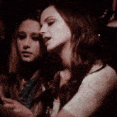 two women are sitting next to each other in a dark room looking at their cell phones .