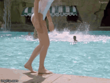 a woman in a bathing suit walks by a pool with a waterfall in the background and a sign that says food & smoothies