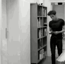 a man is standing in front of a bookshelf holding a book .