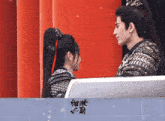 a man and a woman are looking at each other with chinese writing on a wall behind them
