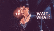 a woman in a black dress is standing in a dark room and says wait what ?
