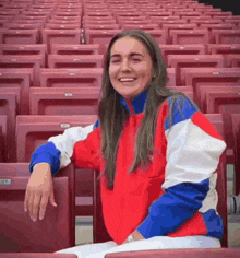 a woman in a red , white , and blue jacket is sitting in a stadium .