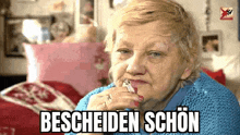 an elderly woman is smoking a cigarette while sitting on a bed with the words bescheiden schön above her .