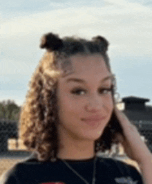 a young woman with curly hair is wearing a black shirt and a necklace and smiling .